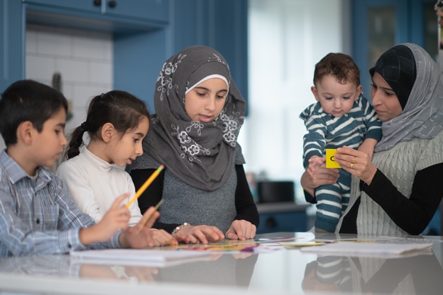 Eine Gruppe muslimische Kinder und Mütter lernen am Küchentisch