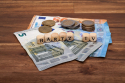 Foto: Eurogeldscheine und Münzen auf einem Holzfußboden und Schriftzug 