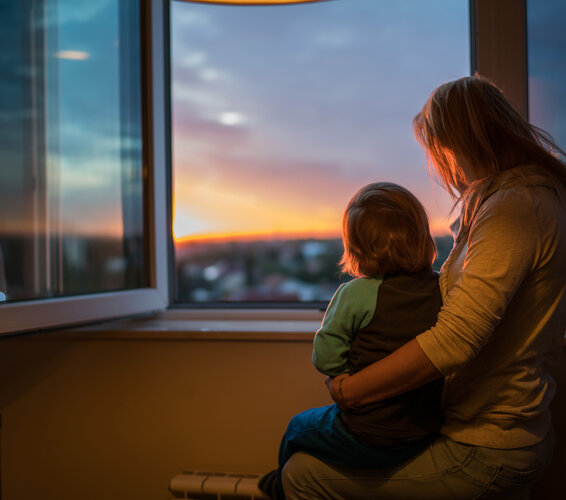 Foto einer Frau, sitzend vor einem Fenster mit ihrem Kind auf dem Arm. – 