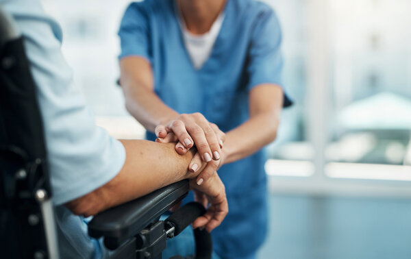 Eine Krankenschwester im blauen Kittel, die einer Person die Hand hält. – 