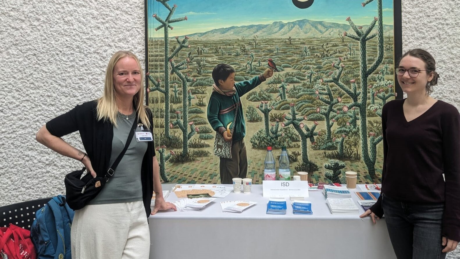 Nadia Wilken und Ina Schmidt am Infostand des Deutschen Vereins. Im Hintergrund ist eine große Zeichnung mit mit einem mexikanischen Jungen in der Natur –
