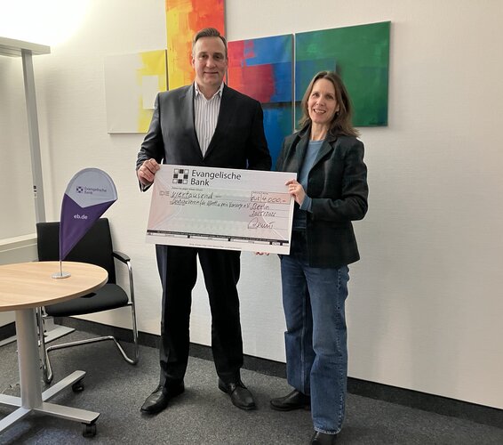 Auf dem Foto sind von links Björn-Olaf Asmus und Dr. Verena Staats zu sehen. Bei stehen und lächeln in die Kamera während eine Förderscheck überreicht wird. – 