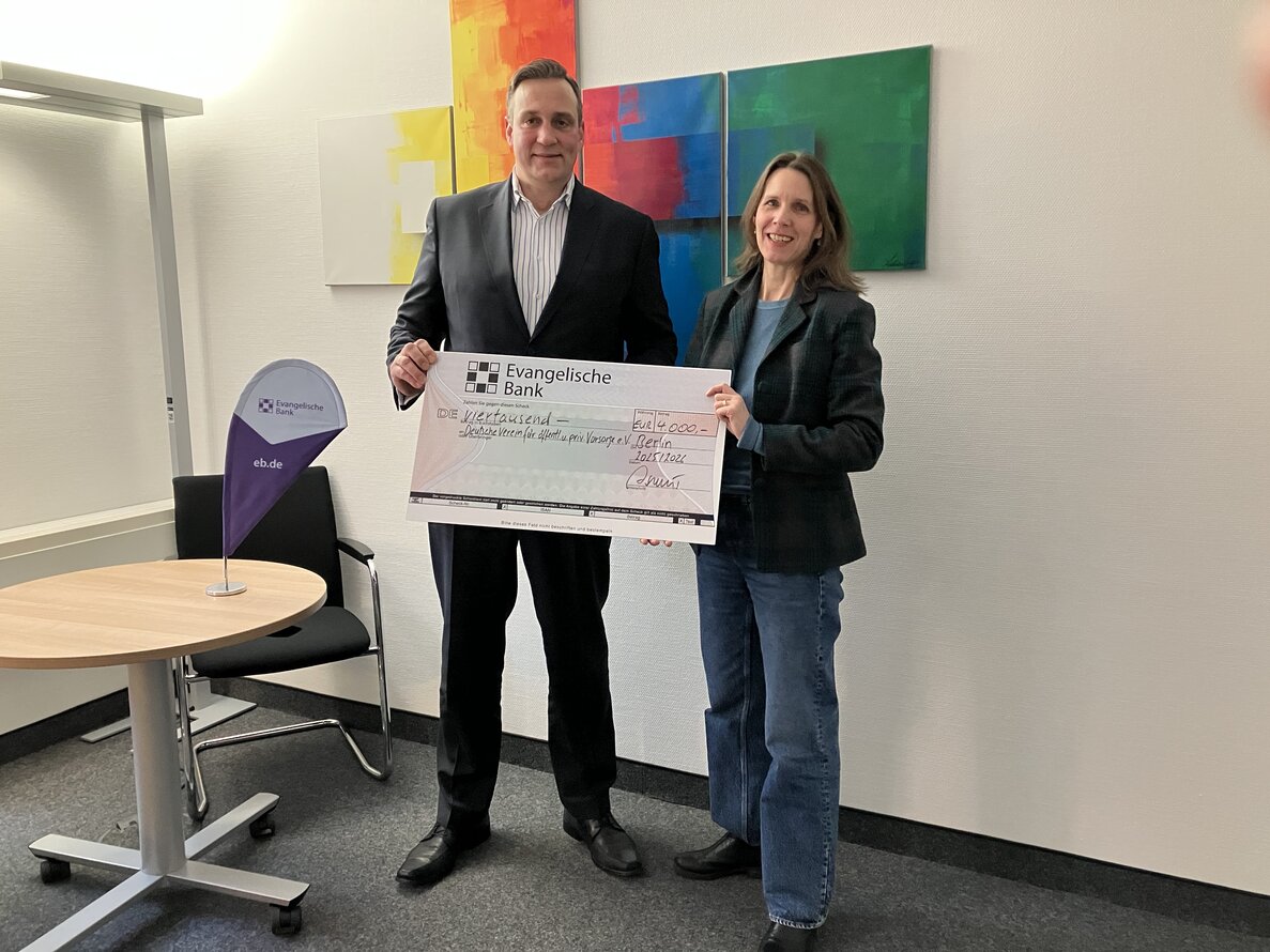 Auf dem Foto sind von links Björn-Olaf Asmus und Dr. Verena Staats zu sehen. Bei stehen und lächeln in die Kamera während eine Förderscheck überreicht wird. – 