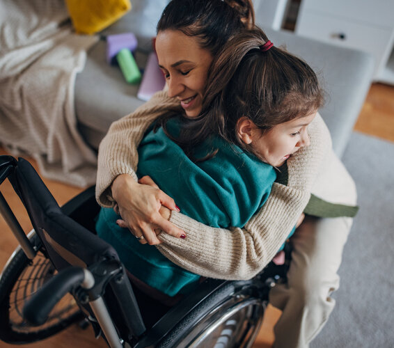 Foto eines Kindes im Rollstuhl, das von seiner Mutter umarmt wird. – 